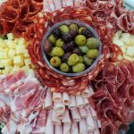 A generous platter with rolled pieces of ham, salami, cubes of cheese and a bowl of mixed olives in the centre.