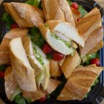 You are looking at a plate of fresh cut baguettes with chicken., salad and cheese.