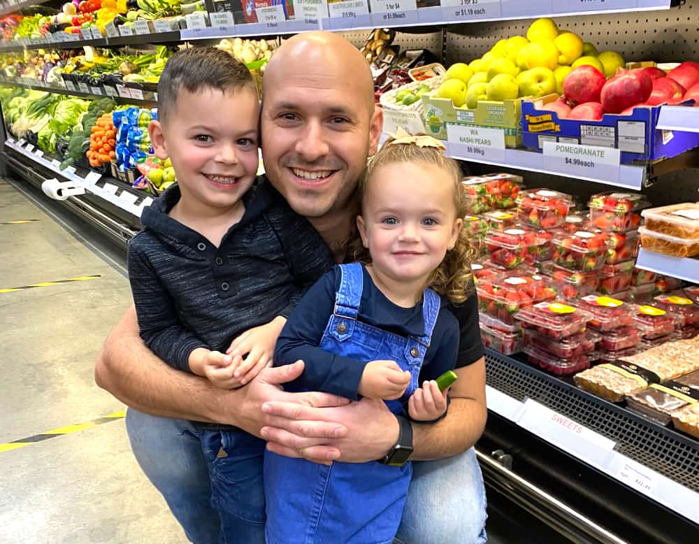 Giusep hugging his two little kids in front of the produce chiller.
